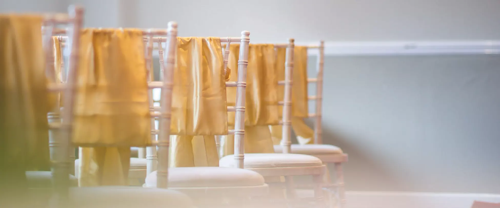 Wooden chairs set up for a wedding ceremony. The chairs have yellow ribbons ties around them..